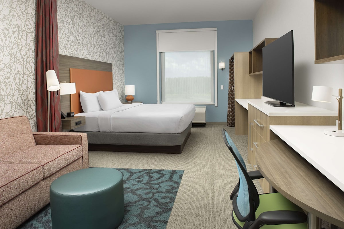 Een hotelkamer met een bed, een bureau, een televisie, een bank en een kamerbreed tapijt met dessin.