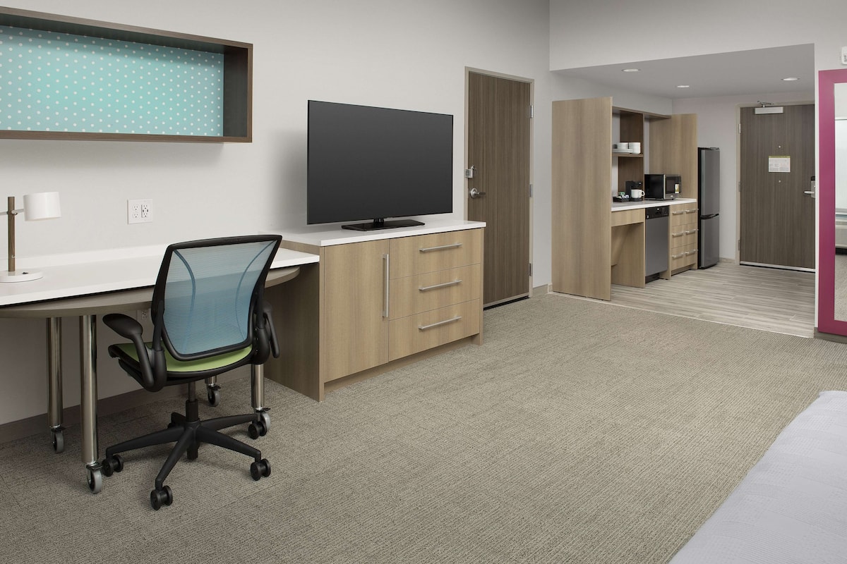 Een moderne hotelkamer met een flatscreen televisie, een bureau met stoel, een kitchenette en een aparte badkamerruimte.