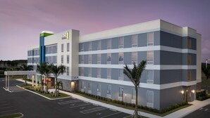 A multi-story hotel with a modern design, featuring a parking lot and a covered entrance area.