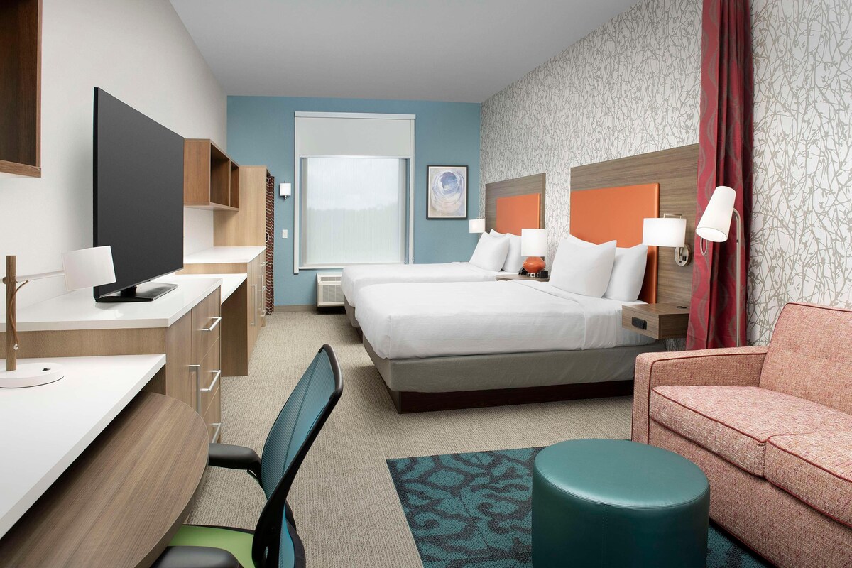 A hotel room with a bed, desk, chair, and a sofa.