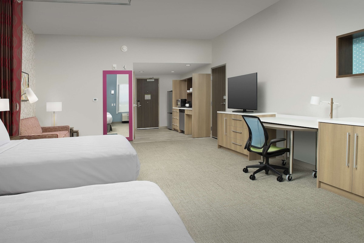 Een hotelkamer met twee bedden, een bureau met stoel, een televisie en een kitchenette.