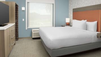 A hotel room with a bed, a television, a nightstand, and a window with blinds.