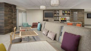 A modern hotel lobby with a seating area, a reception desk, and a flat-screen TV.