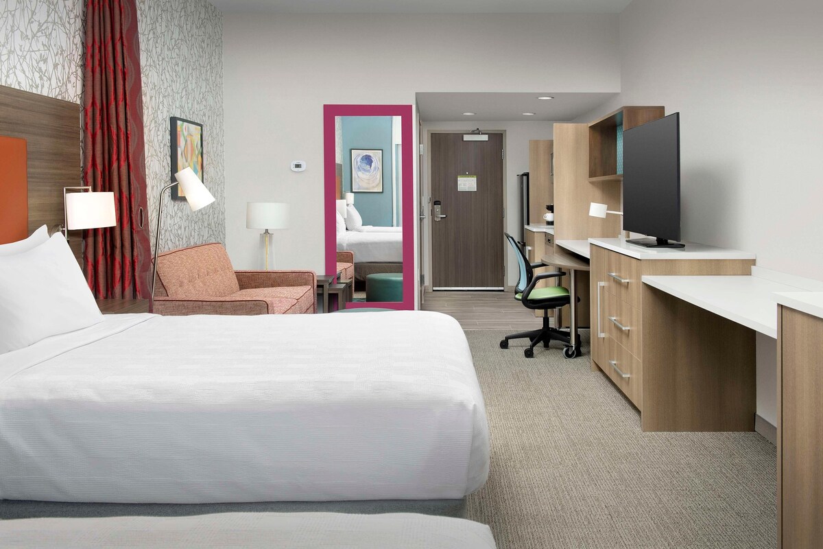 Hotelkamer met twee bedden, een bureau met een televisie, een stoel, een bureaulamp en een deur naar de badkamer.
