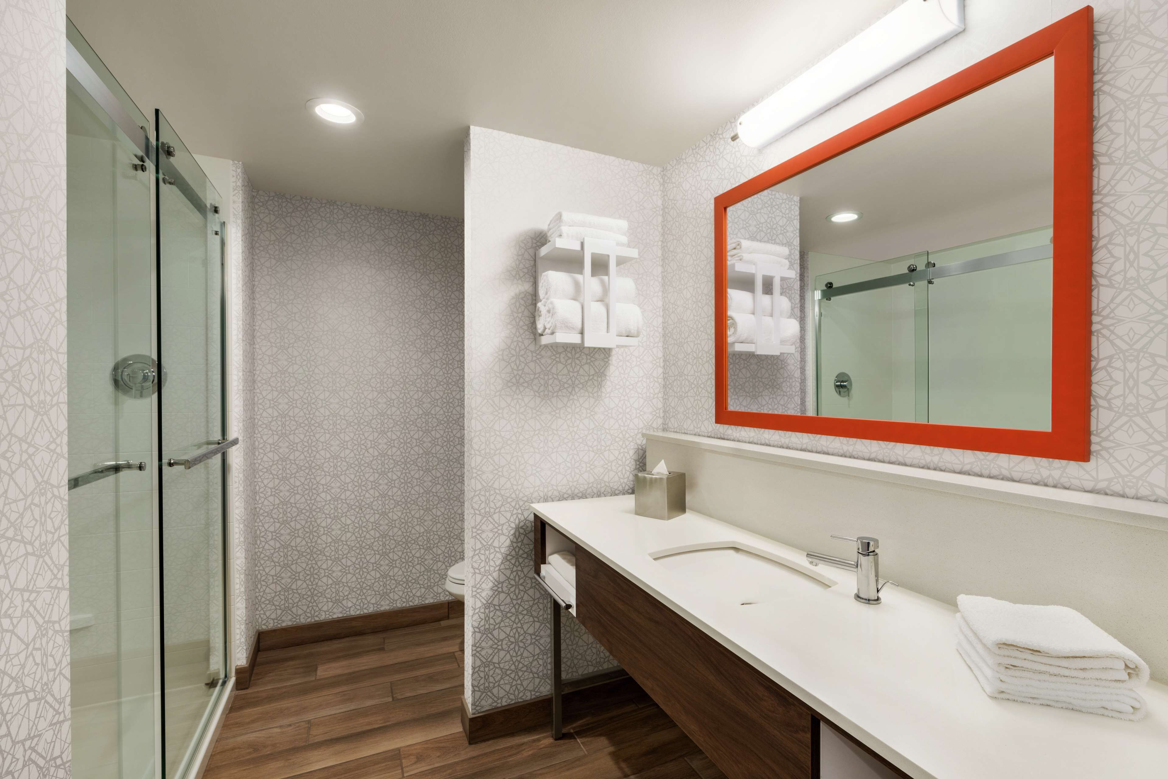 Un baño moderno con cabina de ducha de vidrio, tocador blanco con espejo y un perchero para toallas.