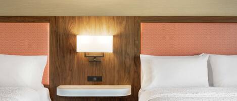 A hotel room with two beds, a wooden headboard, a built-in shelf, and a wall-mounted light fixture.