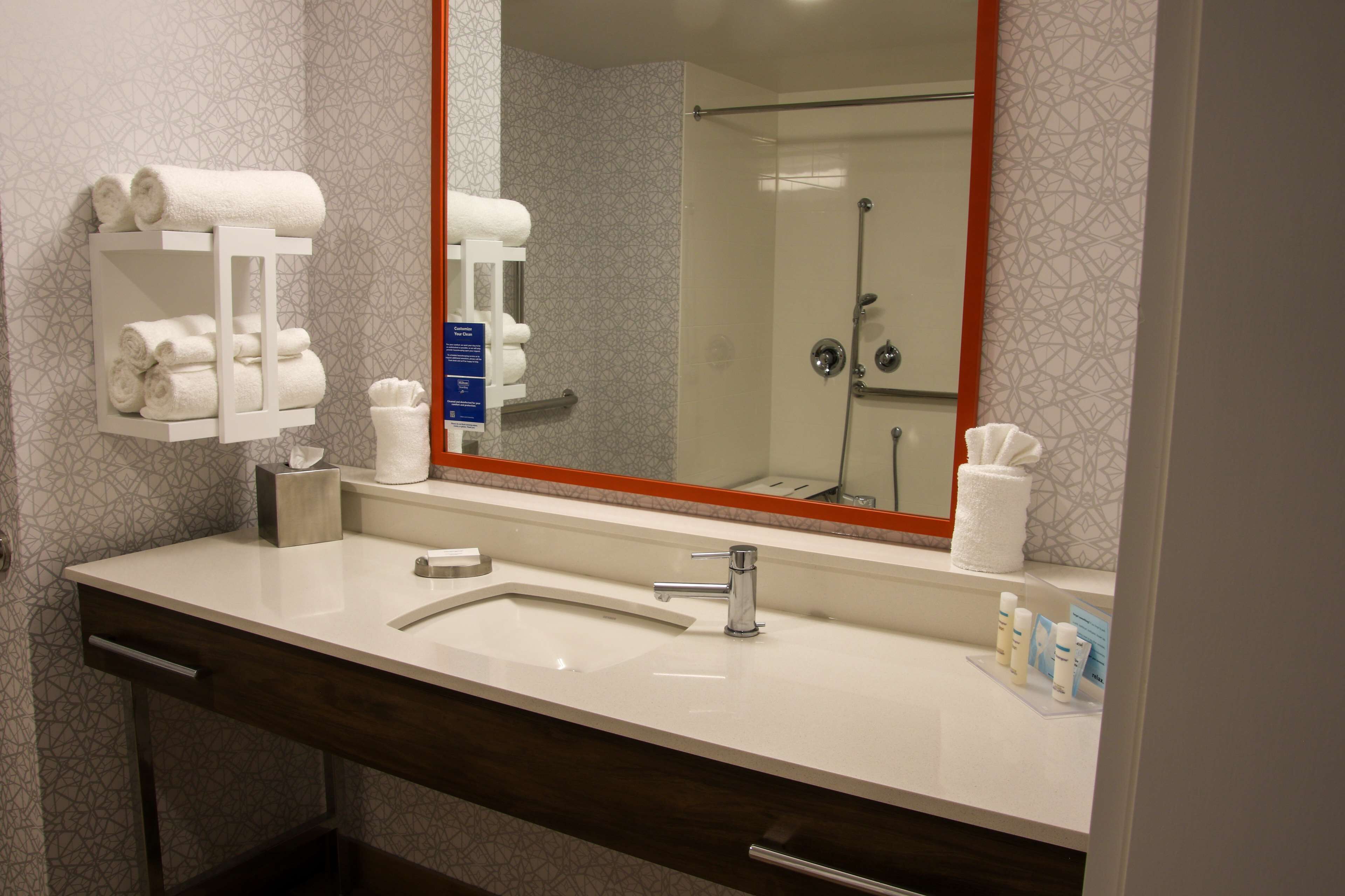A bathroom with a white sink, a large mirror, and a towel rack with towels.