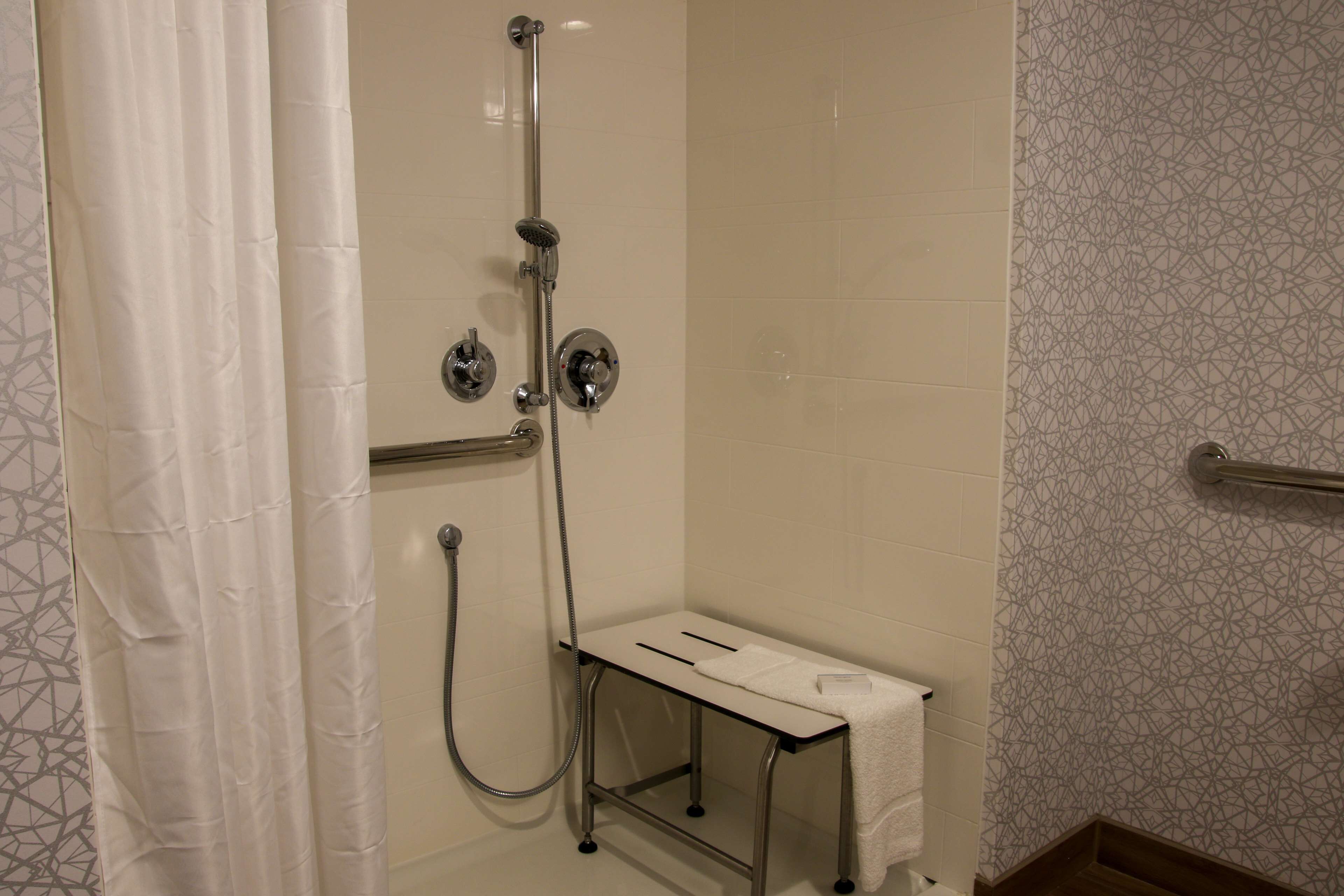 A shower area with a handheld showerhead, a wall-mounted faucet, and a small bench with a towel.
