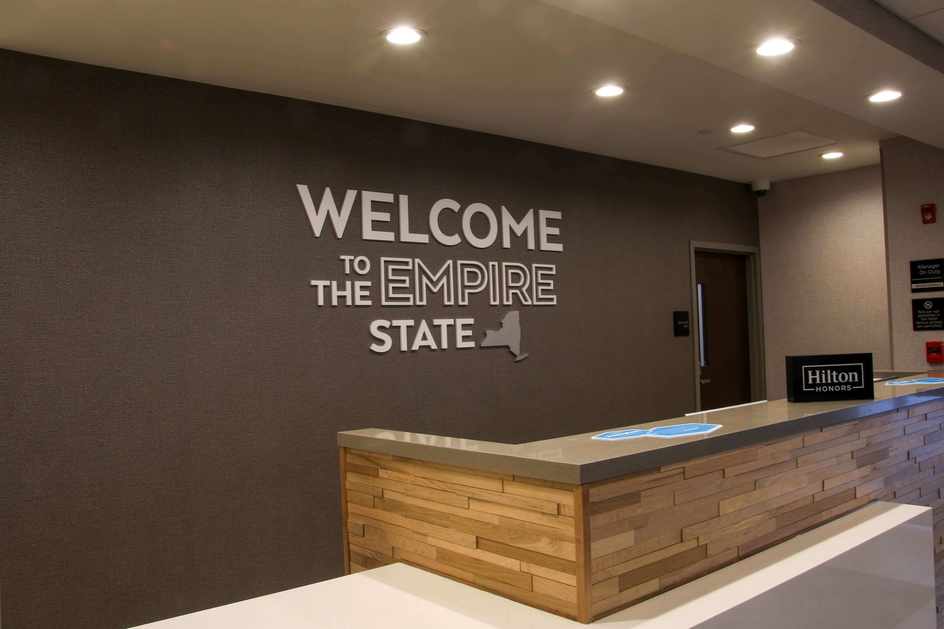 A reception desk with a "Welcome to the Empire State" sign, a wooden counter, and a "Hilton Honors" sign.