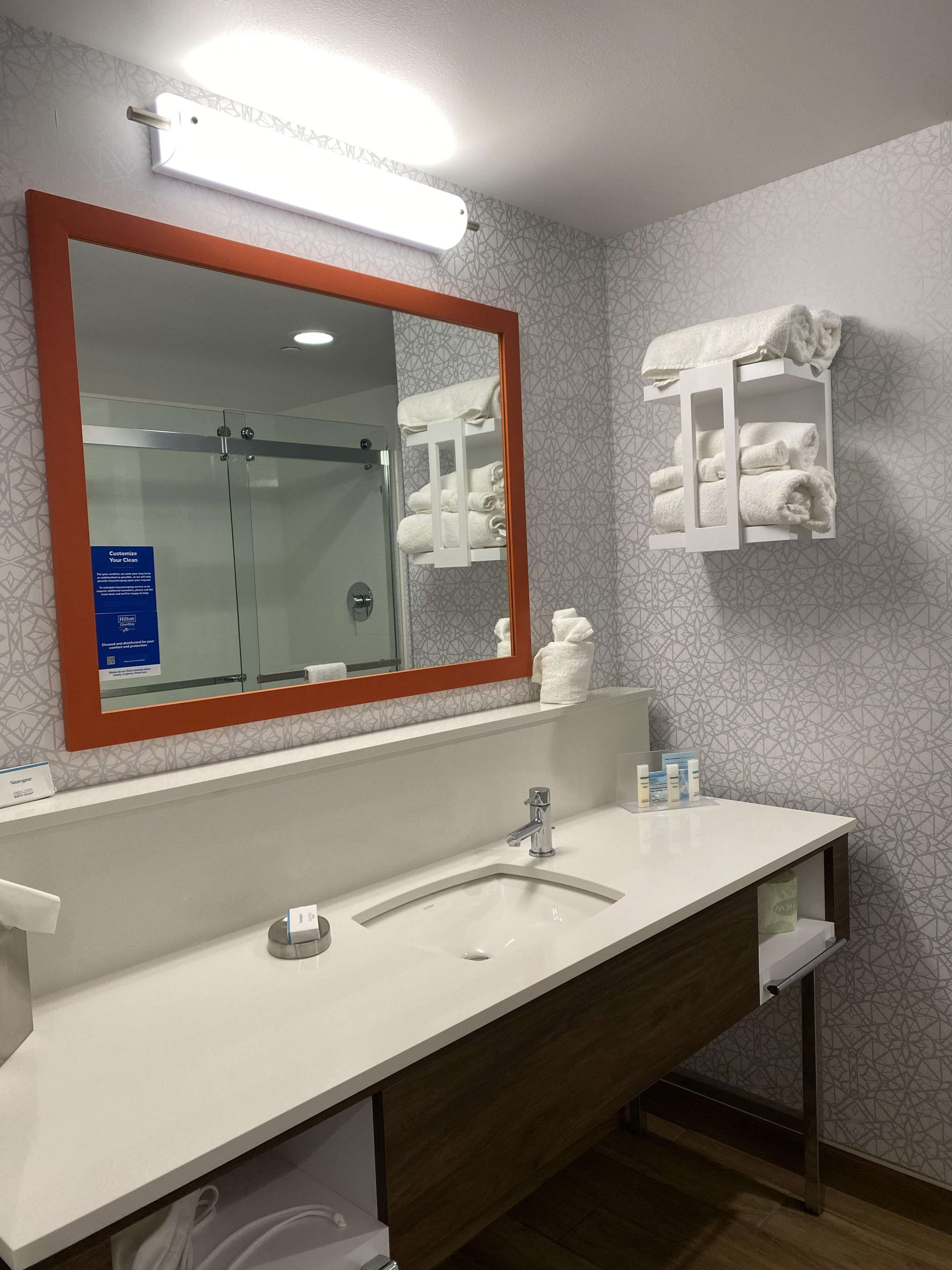 A modern bathroom with a large mirror, a white sink, and a towel rack.