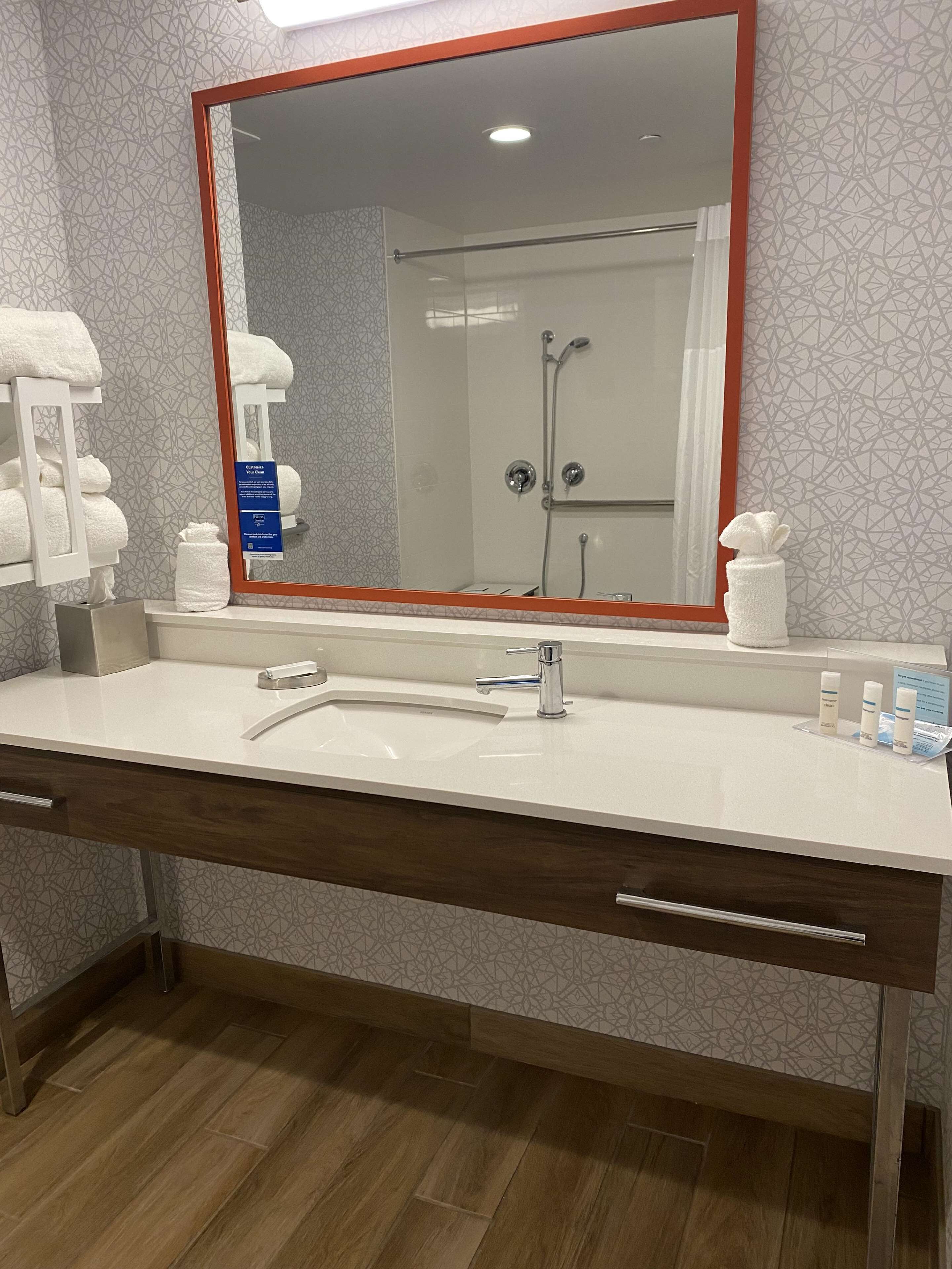 A bathroom with a large mirror, a sink, a shower, and a towel rack.