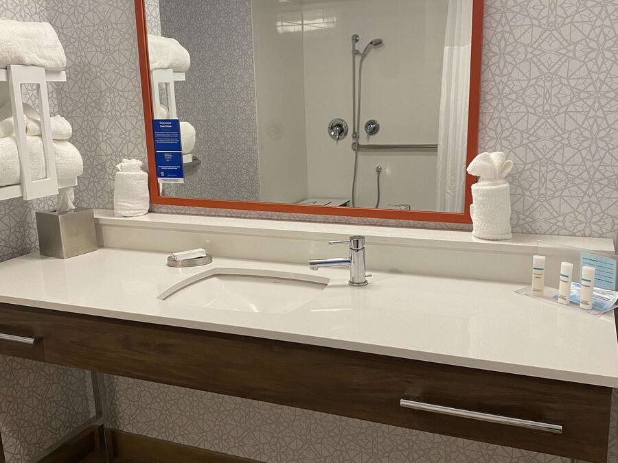 A bathroom with a large mirror, a sink, a shower, and a towel rack.
