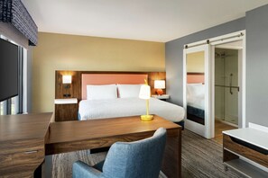 A hotel room with a bed, bedside tables, a desk, a chair, and a shower area.