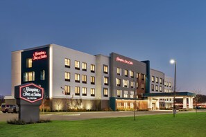 A Hampton Inn & Suites by Hilton building with a modern design, multiple windows, and a well-lit entrance.
