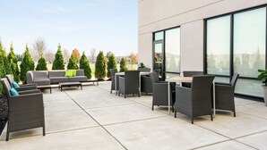An outdoor patio area with a sofa, chairs, and a table, surrounded by potted plants and trees. - Hampton Inn & Suites Olean (Olean)