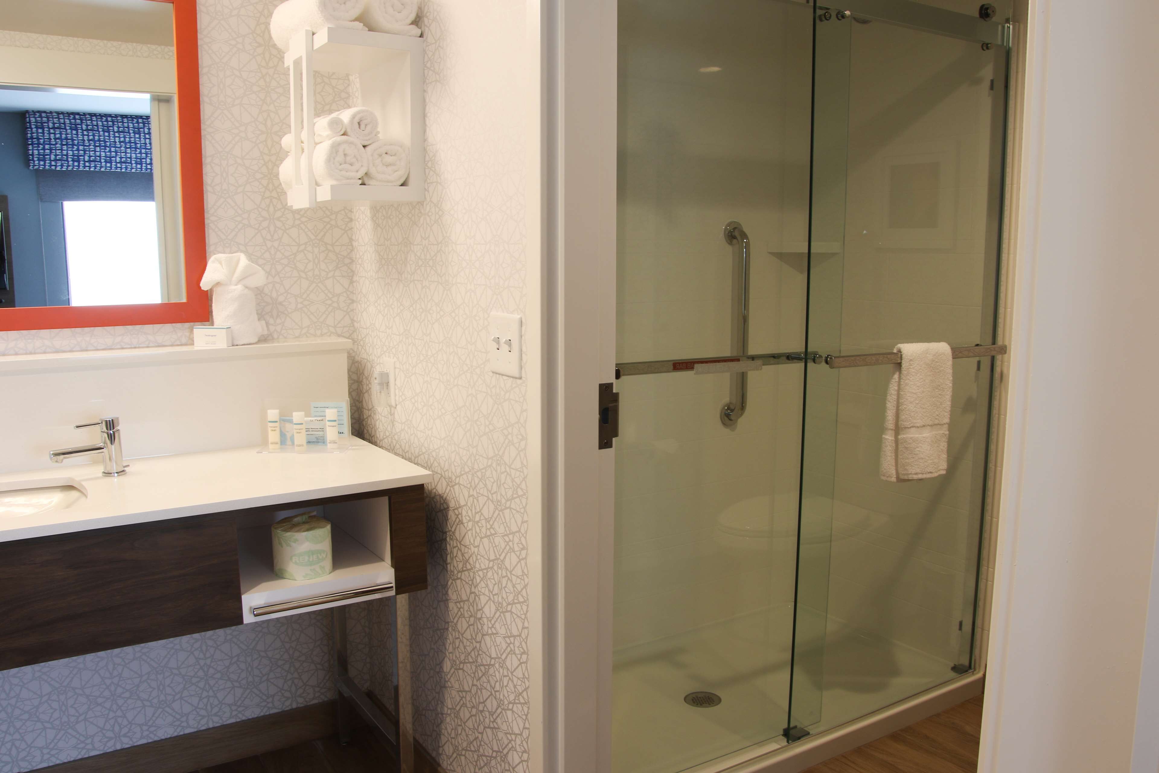 A modern bathroom with a glass-enclosed shower, a white sink, and a mirror with a red frame.
