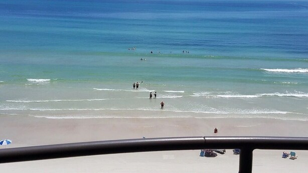 Una playa con gente caminando por la orilla y algunas sombrillas a lo lejos.