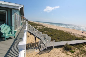 Een strandhuis met een houten terras, een trap naar het strand en uitzicht op de oceaan.