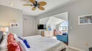 A bedroom with a bed, a ceiling fan, a TV, a dresser, and a window.