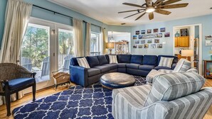A living room with a sectional sofa, a round ottoman, a wicker chair, and a blue patterned rug.