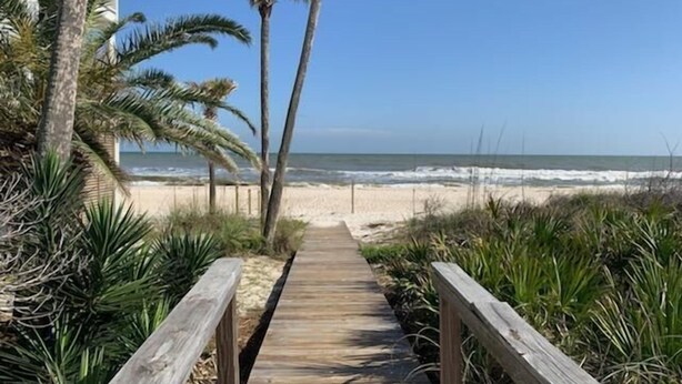 A wooden boardwalk leading to a beach with palm trees and ocean views.