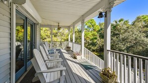 A covered porch with white railings and a row of white chairs.