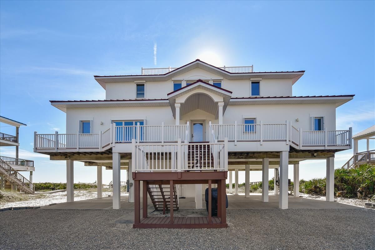 A two-story beachfront house with a covered outdoor area and a staircase leading to the upper level.