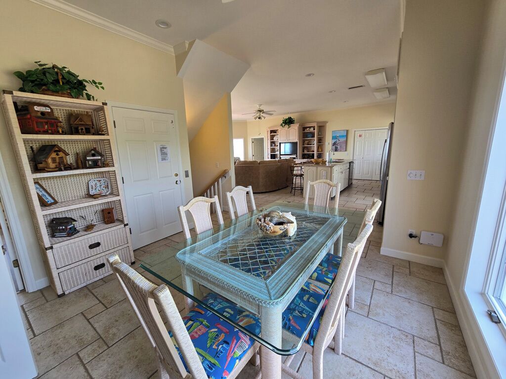 A dining area with a glass-top table, wicker chairs, and a bookshelf filled with decorative items.