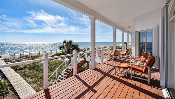 Une terrasse en bois, agréée de mobilier d’extérieur, qui offre une vue sur une plage et l’océan.