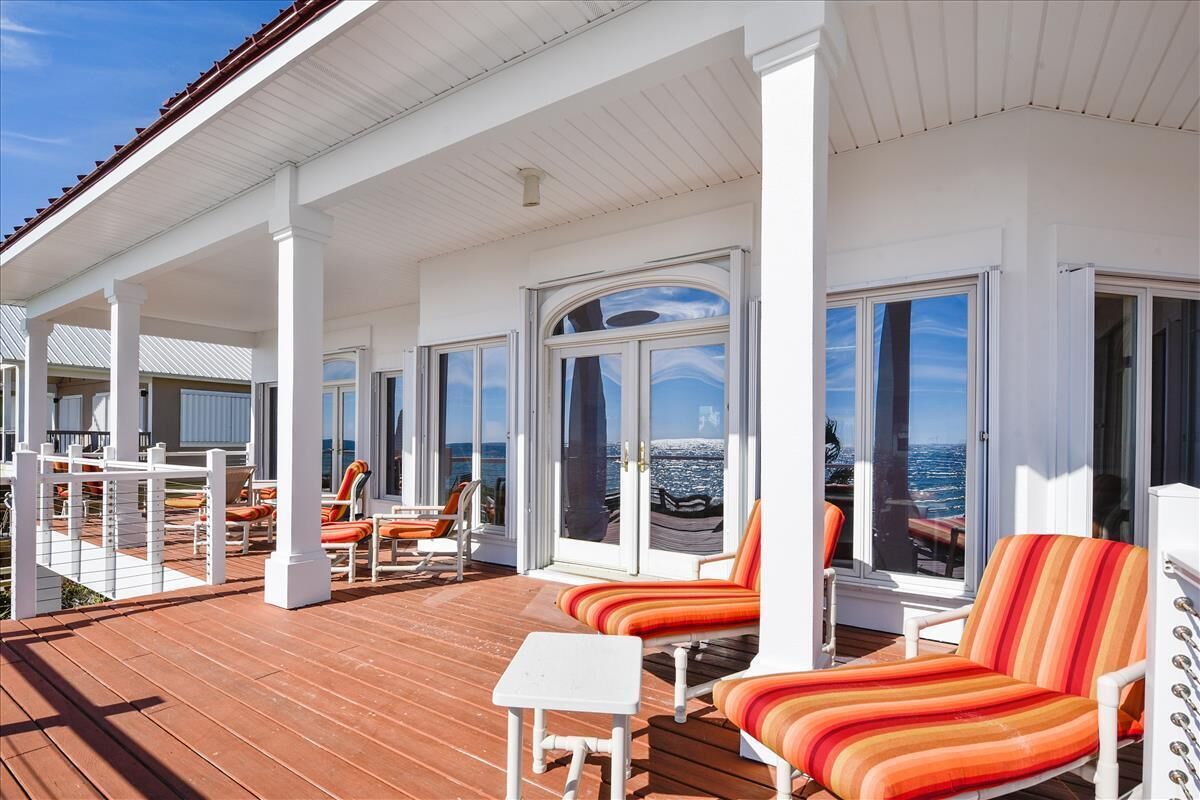 A covered outdoor deck with white columns, orange striped lounge chairs, and a view of the ocean.