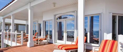 A covered outdoor deck with white columns, orange striped lounge chairs, and a view of the ocean.