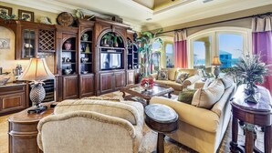 A spacious living room with a large television, comfortable seating, and a view of the ocean through a large window. - Welcome to Deja Vu! (St. George Island)
