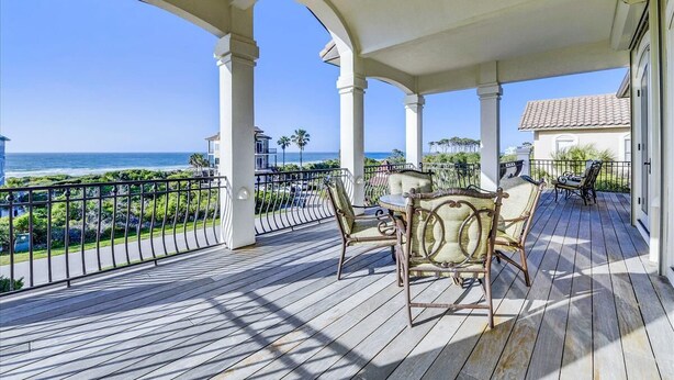 A covered outdoor area with a wooden deck, white columns, and a view of the ocean. - Welcome to Deja Vu! (St. George Island)