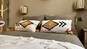 A bedroom with a bed, two pillows with geometric patterns, a wall-mounted mirror, and a decorative wall piece. - "La Calade" Villa les glycines (Collioure)