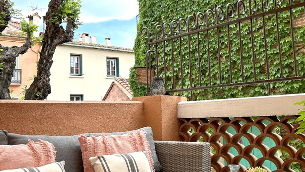 A cozy outdoor seating area with a cushioned sofa, a woven coffee table, and a potted plant. - "La Calade" Villa les glycines (Collioure)