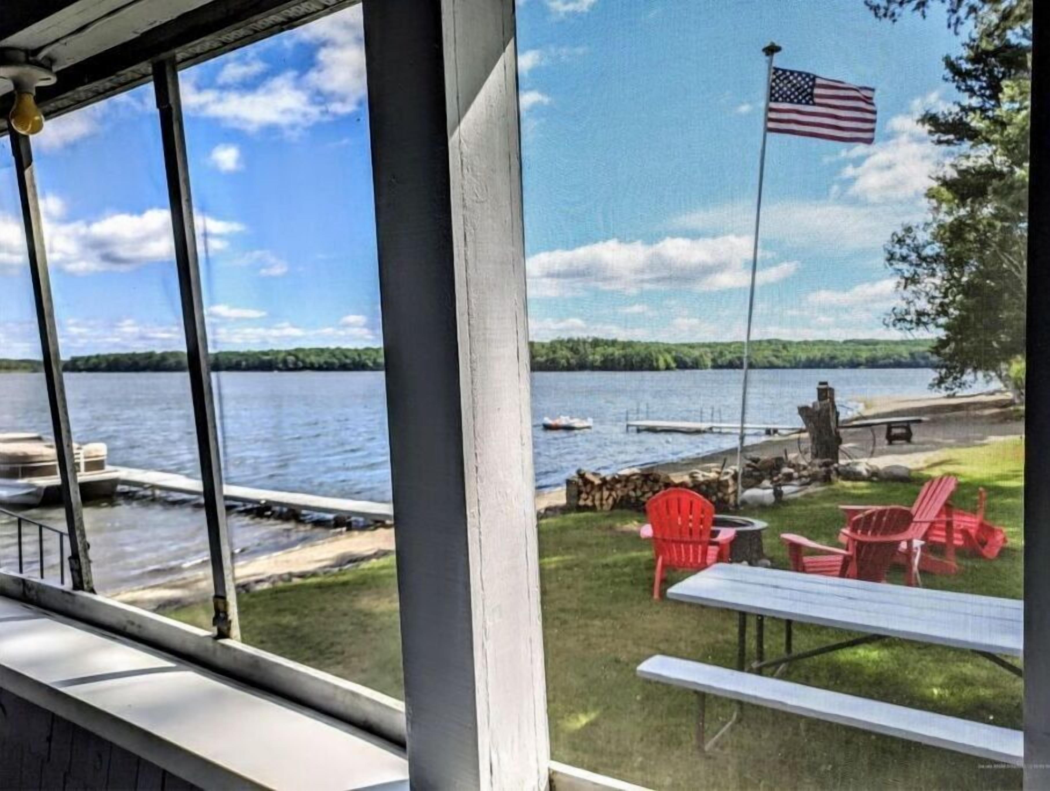 Une vue sur un lac avec un quai, une table de pique-nique et des chaises rouges.