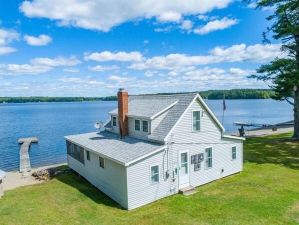 Situated by the water, this house features a gabled roof, chimney, and a small deck area.