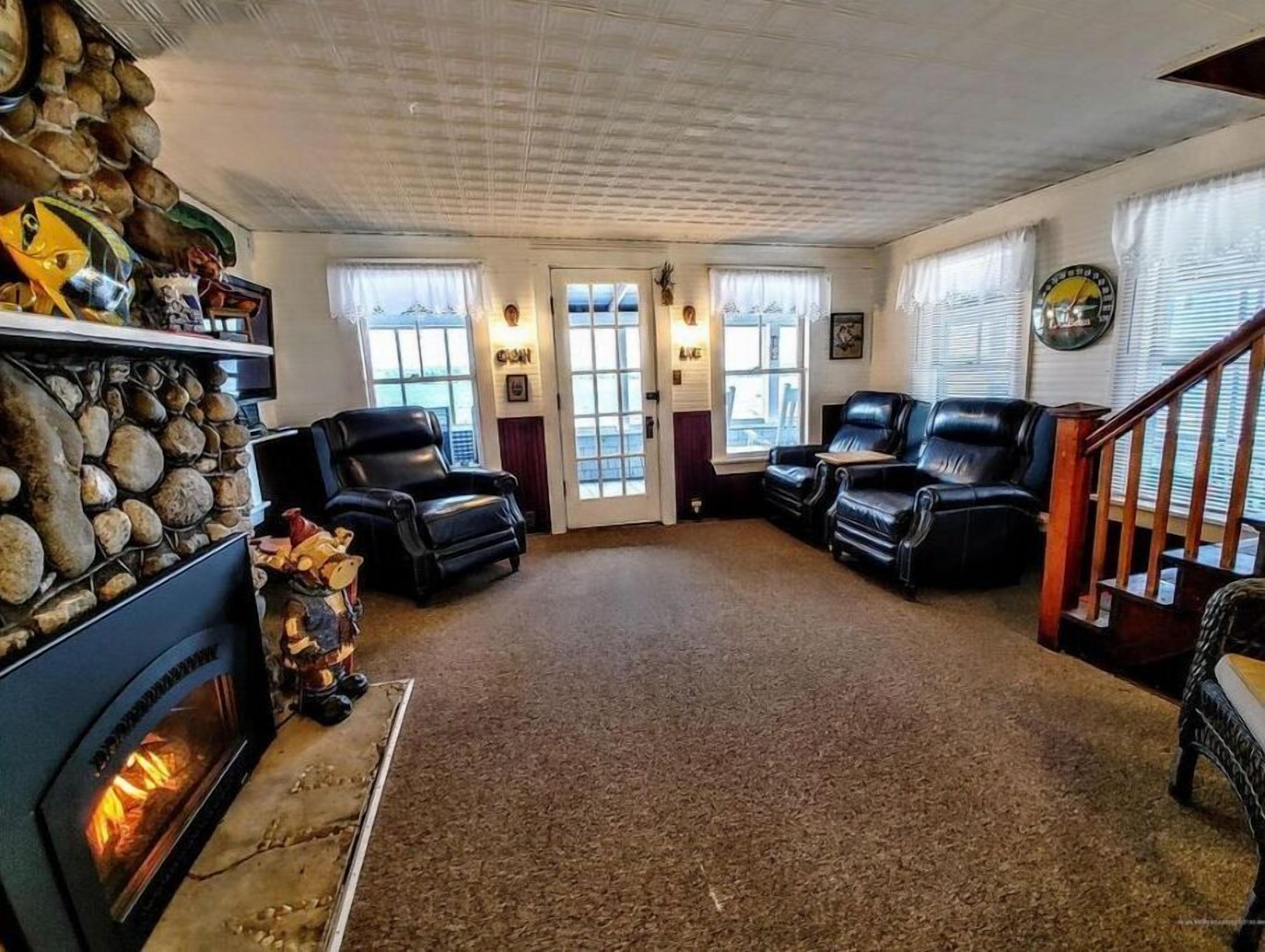 A cozy living room with a fireplace, leather chairs, and a stone wall.