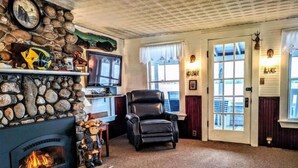 Een gezellige woonkamer met een stenen open haard, een comfortabele leren fauteuil en een televisie aan een stenen muur.