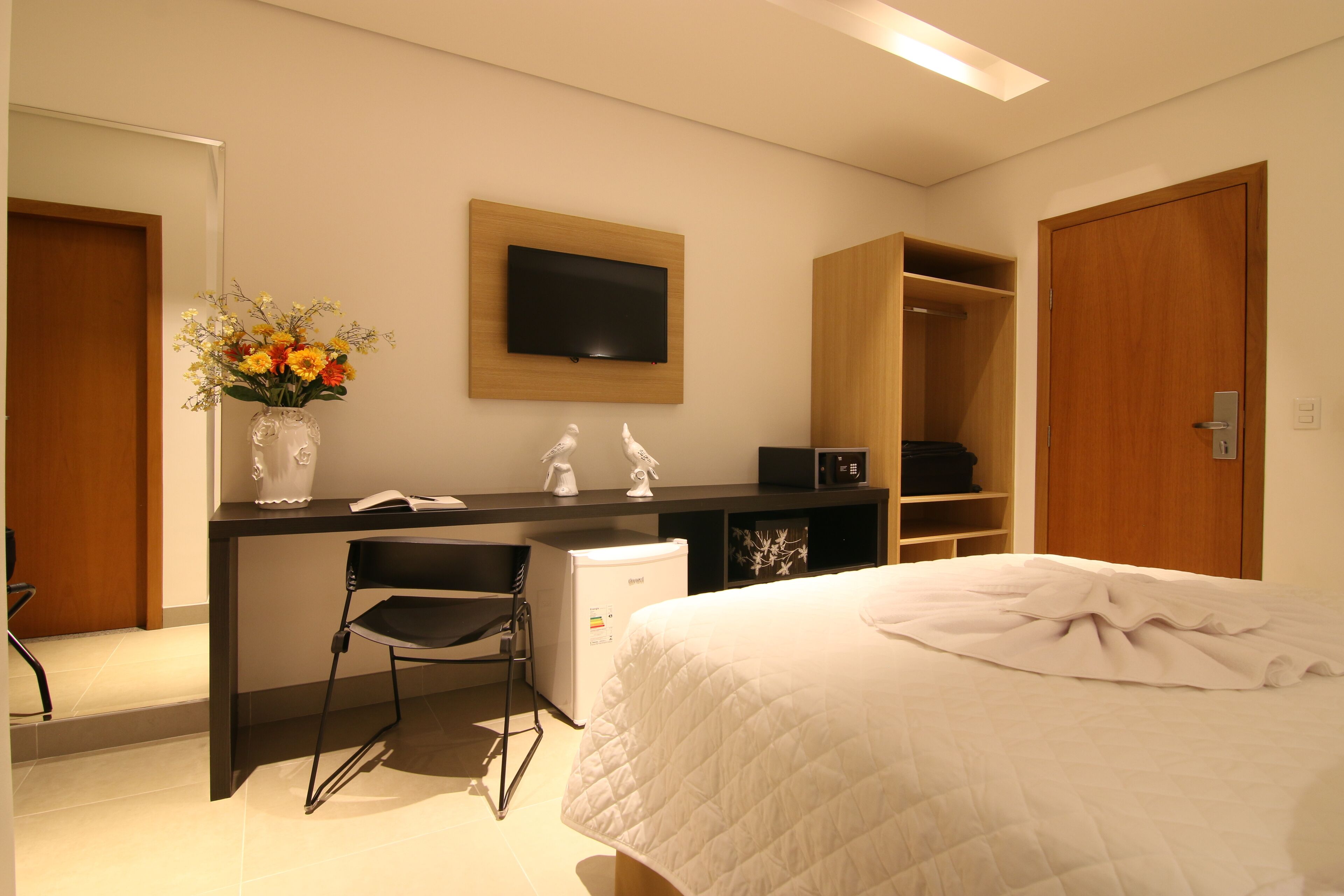 Una habitación de hotel con una cama, un escritorio con una silla, un televisor y un armario.