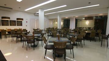 Un comedor amplio con varias mesas y sillas, ventanas grandes y lámparas modernas.