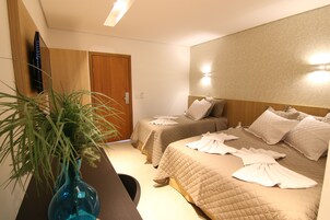 A hotel room with two beds, a TV, a wooden door, and a plant.
