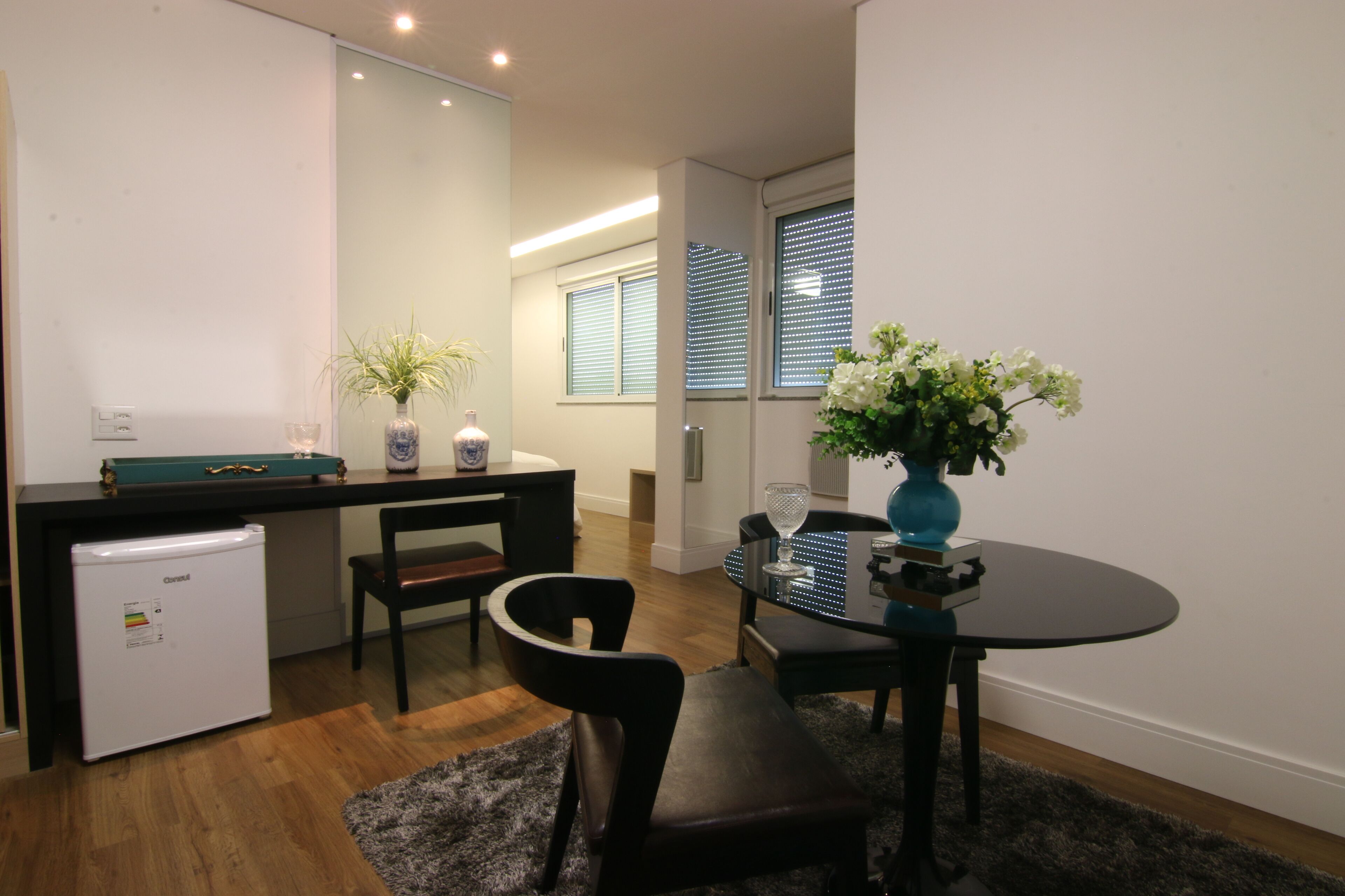 Une cuisine compacte comprenant un réfrigérateur, une table à manger avec des chaises et un petit îlot central agrémenté d’une plante.