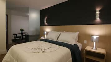 Habitación de hotel con una cama grande, lámparas de noche, una mesita con una silla y un escritorio con una silla.