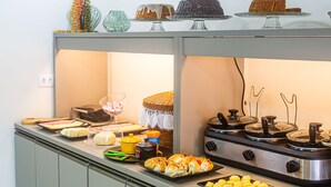 A buffet setup with various food items, a stove, and a wicker basket. - Pousada Maanaim (Ipojuca)