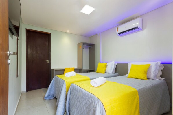 A hotel room with two beds, each with a yellow and white bedspread, and an air conditioning unit on the wall.