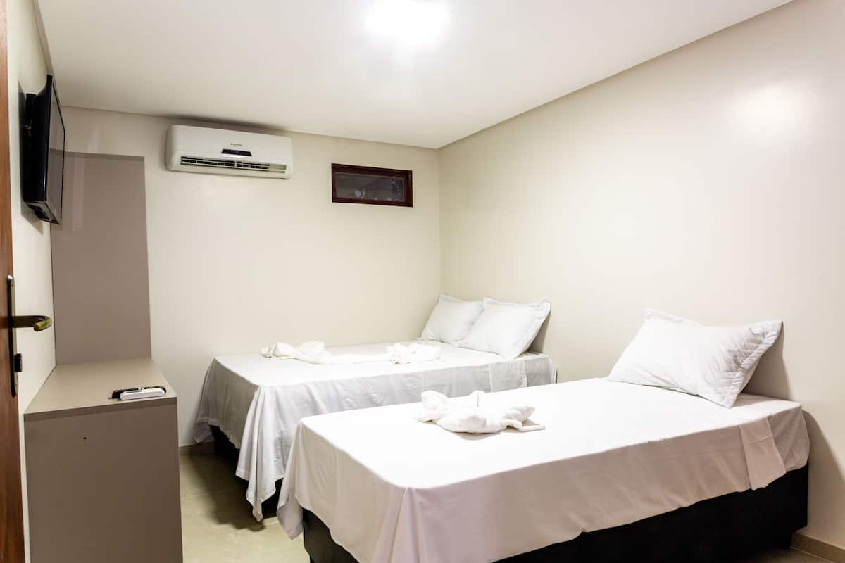 A hotel room with two beds, a TV, an air conditioner, and a small table.
