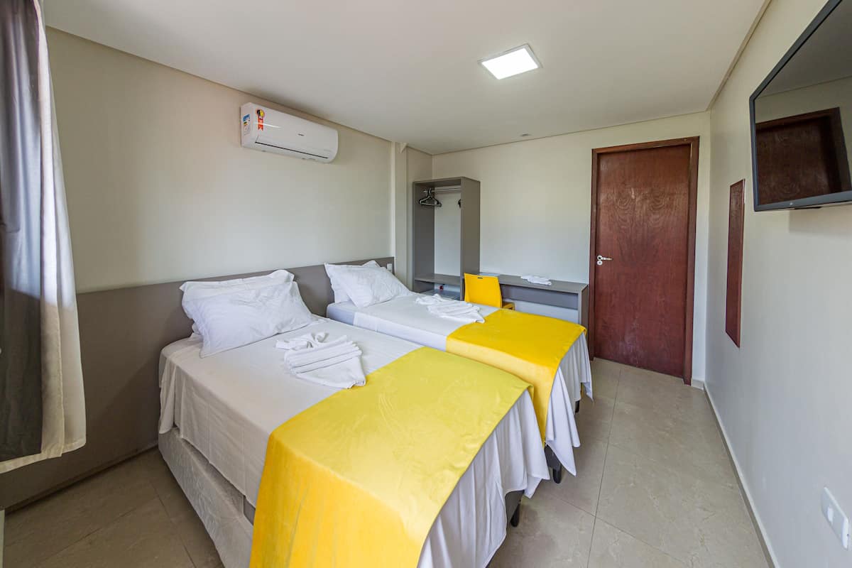 A hotel room with two beds, a mirror, a door, and an air conditioning unit.