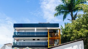 A two-story building with a balcony, a storefront with a bicycle, and a palm tree in the background. - Pousada Maanaim (Ipojuca)