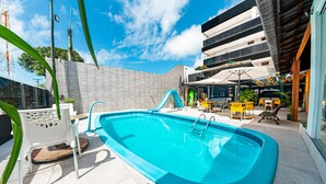 An outdoor swimming pool with a slide, surrounded by outdoor seating and a modern building. - Pousada Maanaim (Ipojuca)